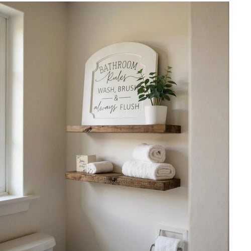 Bathroom with wooden shelves holding towels and a decorative sign on a light-colored wall.